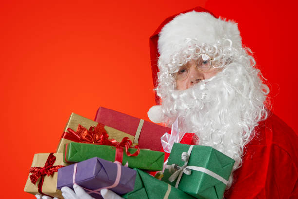 istock Happy Santa Claus with gift boxes in hands on red background with copy space 1334490568