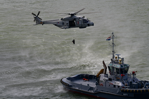 Rotterdam, The Netherlands - September 2019; Close up view of Dutch marine helicopter flying close above water of Nieuwe Maas lifting person from tug boat