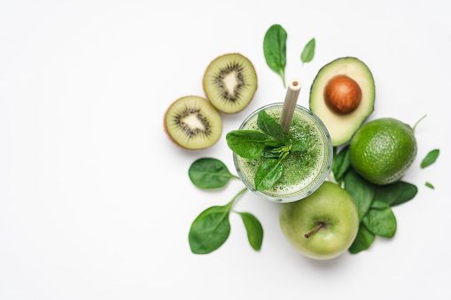 Green smoothie in glass. Spinach, apple, avocado, kiwi, lime ingredients. White background, copy space, top view
