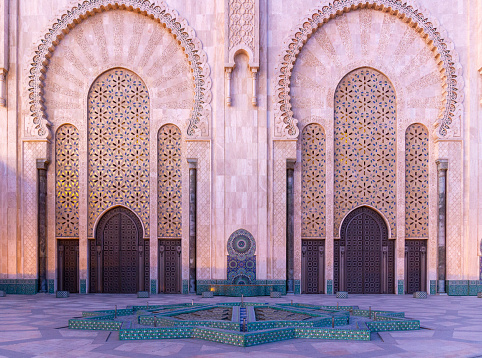 Majestic gate and fountain of Hassan II mosque at dusk in Casablanca, Morocco. Walls with traditional arabic geometric ornament. Islamic culture