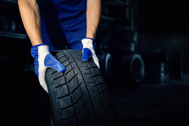 istock mechanic holding car tire on dark workshop background with copy space. tyre service 1334499811