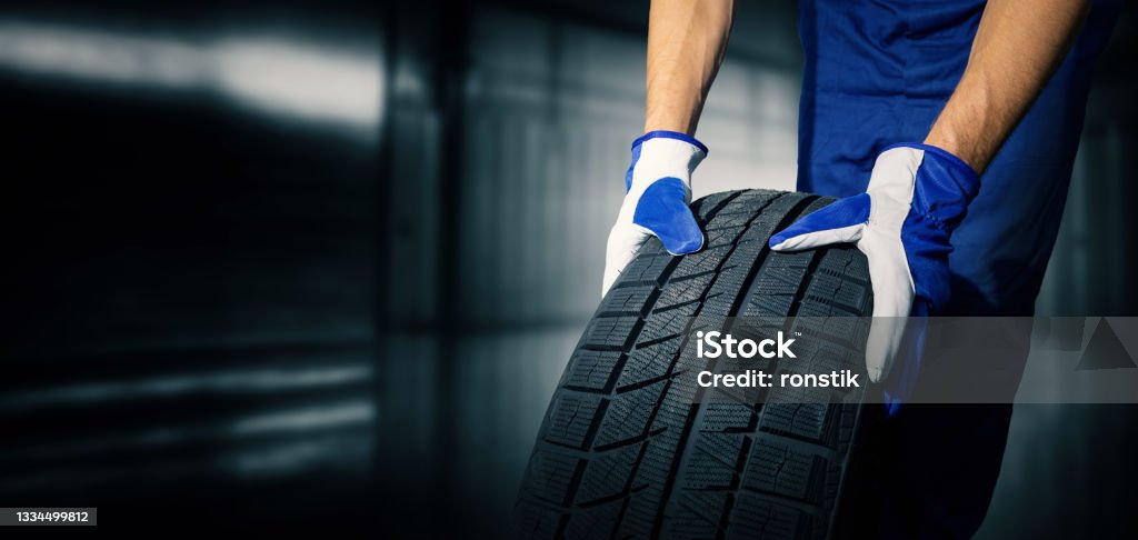 car tire shop and service - mechanic holding new tyre on garage background. copy space Tire - Vehicle Part Stock Photo