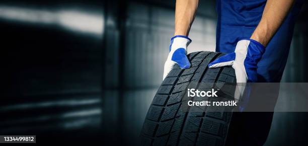 Car Tire Shop And Service Mechanic Holding New Tyre On Garage Background Copy Space Stock Photo - Download Image Now