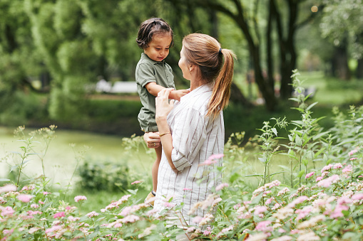 Side view portrait of happy young mother playing with little boy in green park, copy space