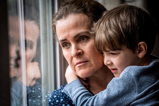 Mature woman posing with her son, very sad looking through window worried about loss of her job due Covid-19 pandemic