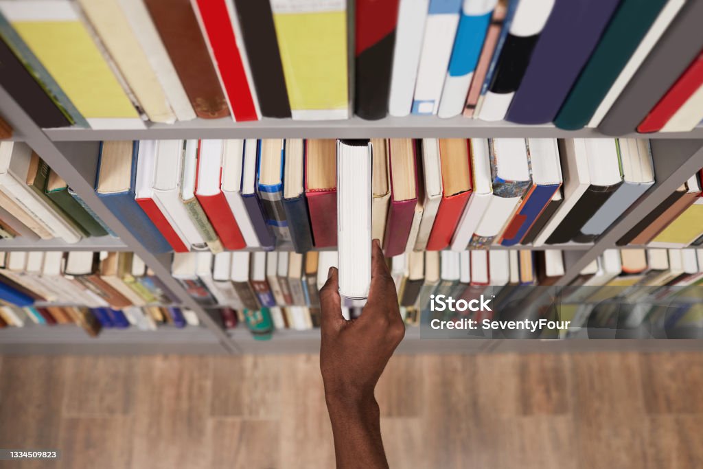 Student Taking Book in Library Closeup Top view close up of male hand taking book off shelf in library, copy space Bookstore Stock Photo