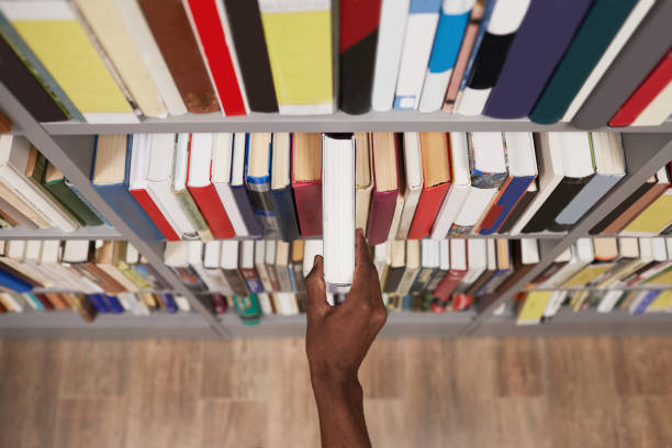 Student Taking Book in Library Closeup Top view close up of male hand taking book off shelf in library, copy space bookstore stock pictures, royalty-free photos & images