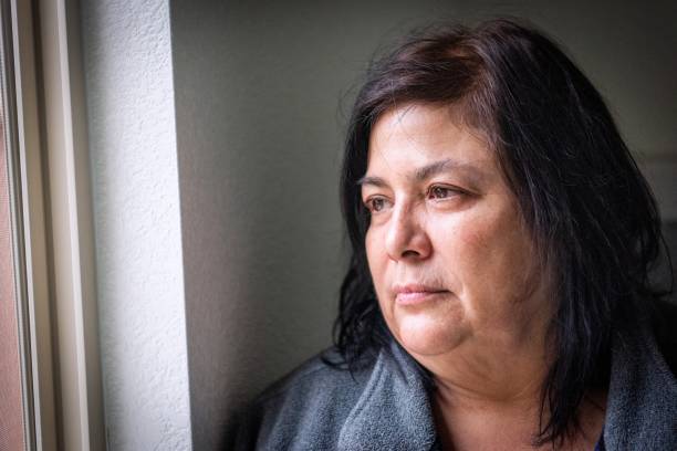 pensive mujer madura, muy preocupada mirando por la ventana preocupada por la pérdida de su trabajo y el desalojo debido a la pandemia de covid-19 - mature adult sadness overweight women fotografías e imágenes de stock