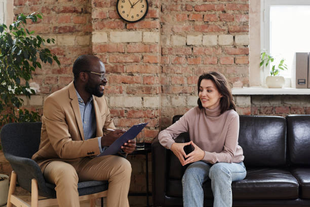istock Smiling young woman sitting on sofa and touching fingers while discussing feelings with psychologist 1334511287