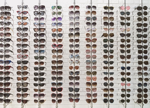 Many sunglasses in eyewear store, display on white wall background