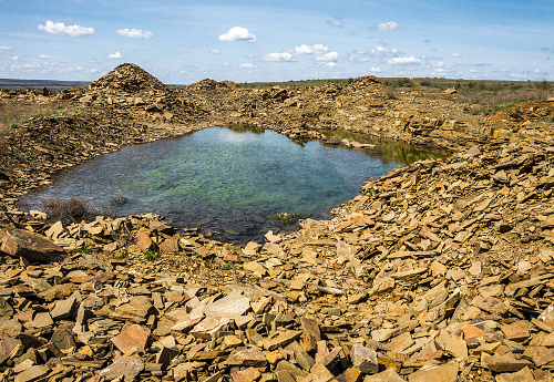 Small lake in the middle of an abandoned slabby sandstone quarry under a blue sky with clouds