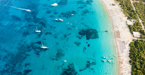 View from above, stunning aerial view of a green coastline with a white sand beach and and boats sailing on a turquoise water at sunset. Cala di volpe beach, Costa Smeralda, Sardinia, Italy. View from above, stunning aerial view of a green coastline with a white sand beach and and boats sailing on a turquoise water at sunset. Cala di volpe beach, Costa Smeralda, Sardinia, Italy. Cala Di Volpe stock pictures, royalty-free photos & images