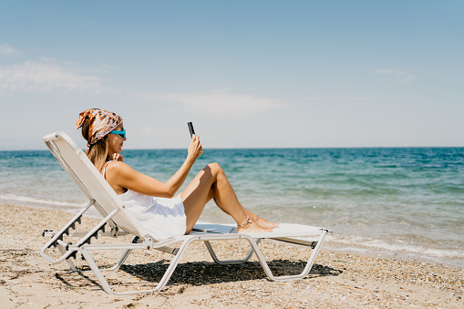 Woman using laptop and the phone at the beach