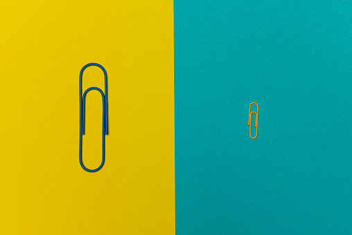 Big paperclip and standard paperclip on the two color background.