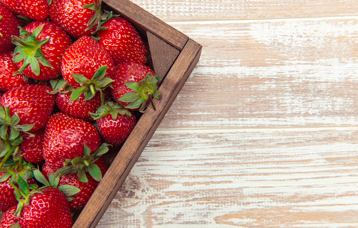 Fresh strawberries in a wood container on the white wooden table.