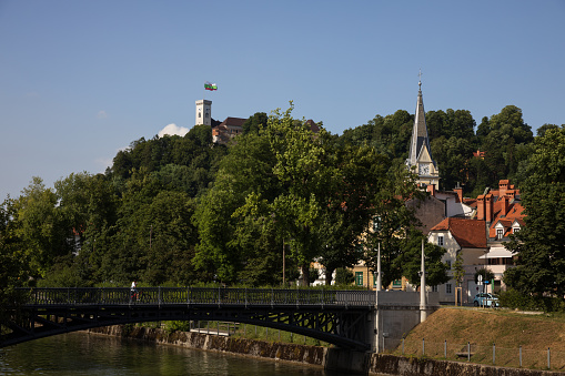 Ljubljana, Slovenija - July 12, 2021: Hradeckega bridge over river Ljubljanica with the castle of Ljubljana capital of Slovenia in the background.