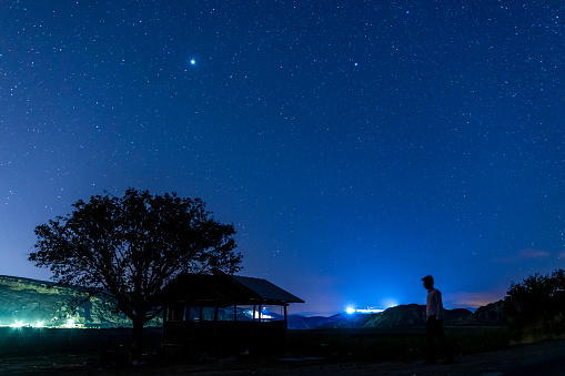 Yıldız manzarasında ağaç altında bulunan kulübesine doğru yürüyen bekçi. gece karanlığında uzun pozlanmış fotoğraf, full frame makine ile çekilmiştir.