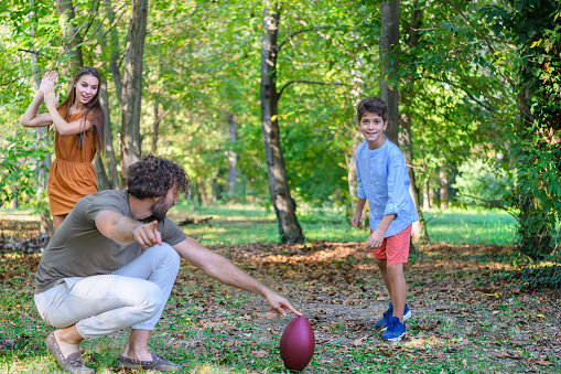 Young Parents and Cute Kids are Smiling and Enjoying in Time Together While Playing American Football During a Warm Sunny Day.