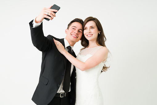 We got married. Caucasian couple taking a selfie together. Bride and groom posting a picture on social media at her wedding day