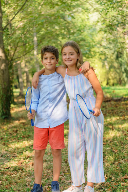 a young boy is ready to play badminton at the playground with his cute little sister. - tennis teenager little boys playing imagens e fotografias de stock