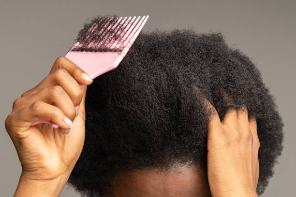 Close up of African female using comb, brushing curly trick hair isolated on studio gray wall. Close up of African American woman using pink plastic comb over studio gray wall background. Unrecognizable black girl brushing curly trick hair, Haircare, daily routine concept. combing stock pictures, royalty-free photos & images