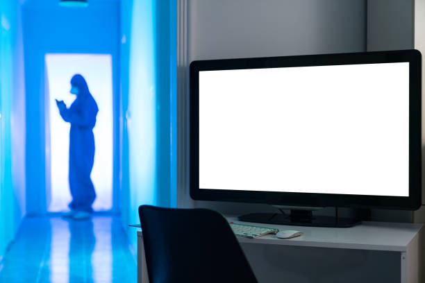 Radiologist doctor wearing a blue hazmat suit, protective face mast and protective gloves working in radiology clinic. A monitor of computer with white color for copy space is seen on the right side of frame. Shot indoor with a full frame mirrorless camera.