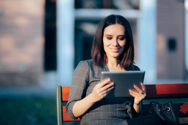 istock Woman Sitting on a Bench in the Park Holding a PC tablet 1334546421