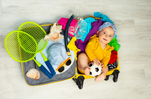 Little baby girl lay in the ready for travel suite case hand luggage with soccer ball