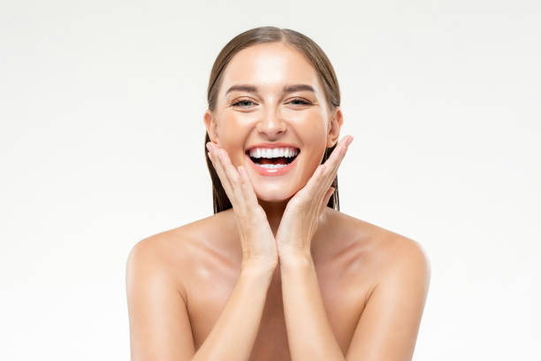 foto de belleza de una joven y sonriente mujer caucásica positiva con las manos tocando la cara en un fondo de estudio blanco aislado - head shoot fotografías e imágenes de stock