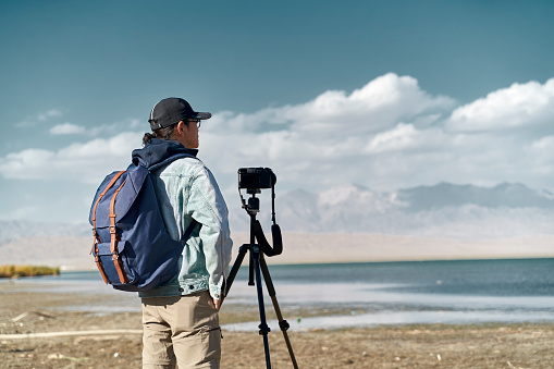 asian photographer standing by a lake looking at view observing