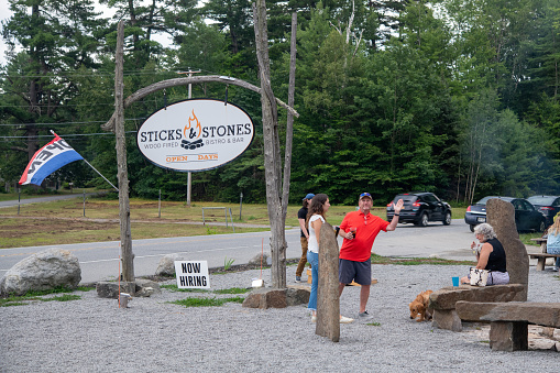 Schroon Lake, USA - August 7, 2021. People enjoying their drink at front yard at Sticks & Stones restaurant with man waving to photographer in Schroon Lake in Upper New York, USA