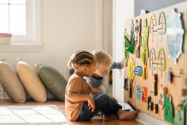 Nursery school friends learning togethehr Two toddler boys rearrange objects on the wall with focus and curiosity. playroom stock pictures, royalty-free photos & images