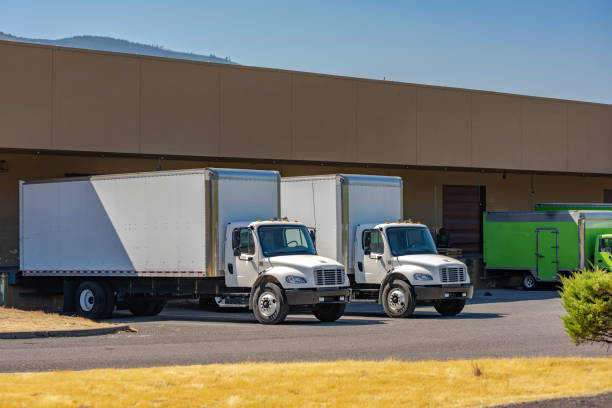 istock Compact medium size rig day cab semi trucks with long box trailers for local delivery standing at warehouse dock loading commercial cargo 1334557346