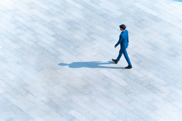 トップ航空写真のビジネスマンは、地面に黒いシルエットの影、社会静物の概念で歩行者のコンクリートを横切って歩きます。 - 人 歩く ストックフォトと画像