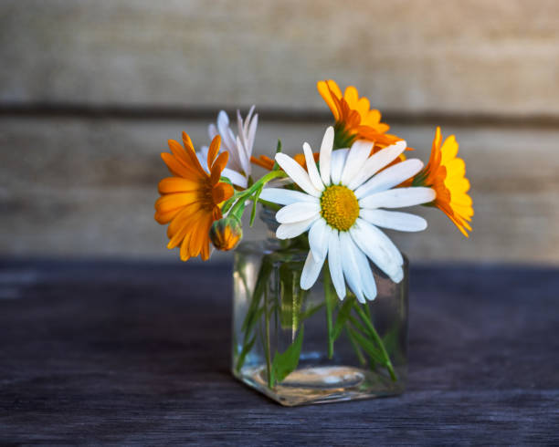 istock Small bouquet with chamomiles and calendula in a glass jar on the table 1334565501