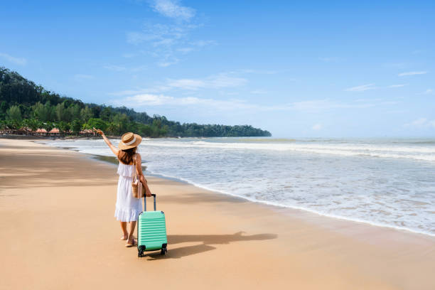 Young woman traveler with luggage relaxing and enjoying on tropical beach in sunny day, Summer vacation and travel concept stock photo