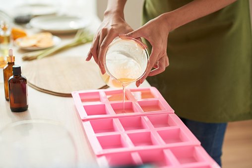 Close-up image of woman pouring melted soap with essential oils into plastic form