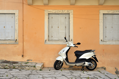 White scooter parking at the wall of the building. Scooter standing at the empty street of old Mediterranean town