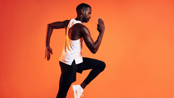 istock Side view of a male runner sprinting over orange background 1334580209
