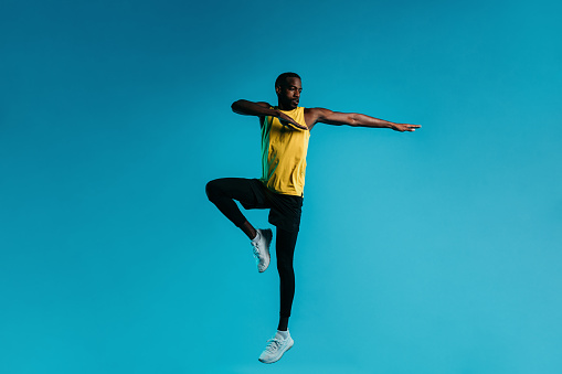 Young man in sportswear jumping and stretching his arms over blue background