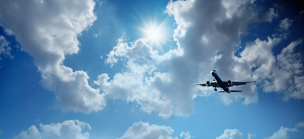 Transportation image of flying commercial passenger airplane over the cloudy sky with sunny blue sky with shining sun