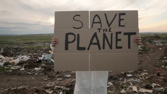 person wearing protective costume and mask holding poster with save the planet slogan iroi