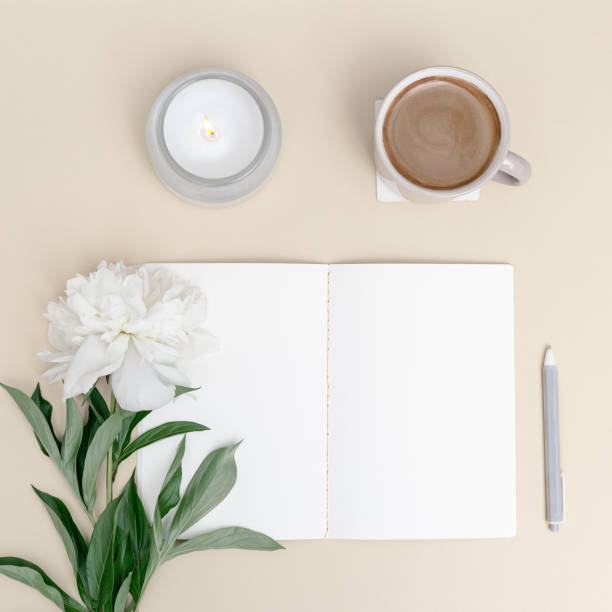 istock Top view of notebook, white peony flower, cup of cofffee on table. Creative workspace minimal style with aroma candle for comfort work 1334585404