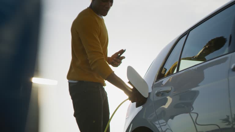 SLO MO young man uses his smartphone while he waits for his car to be charged