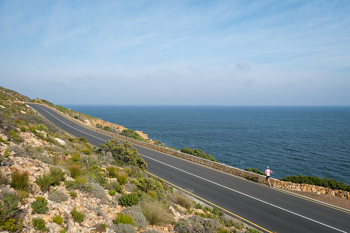 A fit woman runs along a beautiful coastal road overlooking the ocean. Woman enjoys an active and healthy lifestyle.