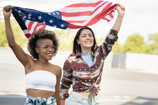 Afro woman and white woman are holding the U.S.A flag very happy
