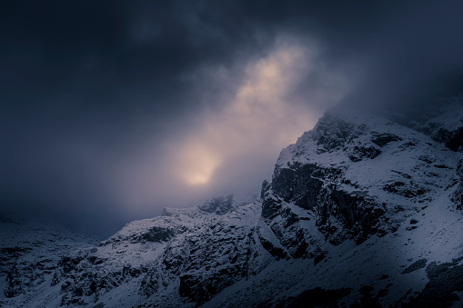 Dramatic Kościelec Peak view, High Tatra Mountains, Poland. Dark winter day, sunlight behind the cloudscape. Selective focus on the rocks, blurred background.
