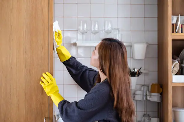 A housewife wearing protective glove, cleaning wooden cupboard in the kitchen at home