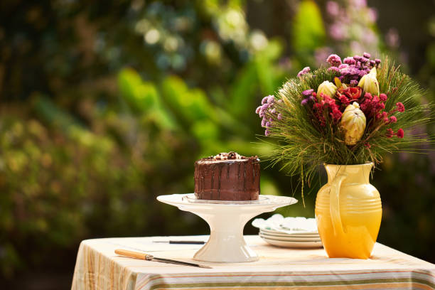 Chocolate wedding cake sitting with a bouquet in a vase outside on a table for a wedding reception