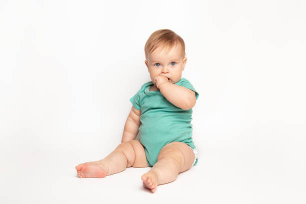 cute Caucasian one year old baby sucks thumb and scratches his first teeth. toddler boy teasing on white background in studio. baby care and child health concept cute Caucasian one year old baby sucks thumb and scratches his first teeth. toddler boy teasing on white background in studio. baby care and child health concept. baby1 stock pictures, royalty-free photos & images